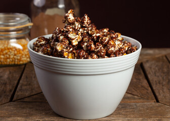 Sweet or sugared popcorn with chocolate or cocoa on wooden table and ingredients in the background.