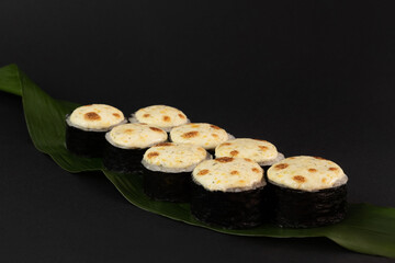 Baked sushi with salmon, avocado, red caviar and baked cream cheese cap, on a banana leaf on a black background. Delicious traditional Japanese food with sushi rolls.