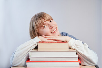 Attractive blonde student or school girl relaxing lying on stack of books and smiling. Young female with books in class with copy space. Homeschooling or back to school concept. High quality photo