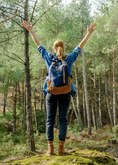 Back view at young tourist woman with backpack and raised hands.