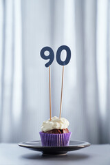 Homemade chocolate tasty cupcake with creamy topping and number 90 ninety on black plate and bright...