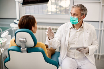Dentist using touchpad and talking to female patient during appointment at dentist's office.