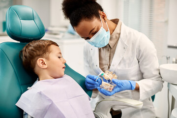 African American dentist teaching small boy how to brush teeth properly during dental appointment.