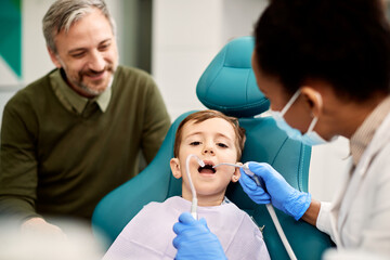 Little boy having dental check-up while being with his father a dentist's office.