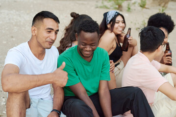 Group of cheerful friends dressed in summer clothing toasting with beer bottles at the beach