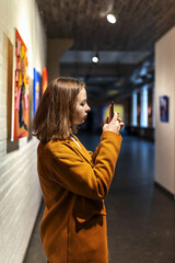 Young teen girl photographs a picture on a smartphone in an art gallery
