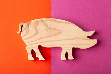 A figurine of a pig carved out of solid pine by a hand jigsaw. On a multi-colored background