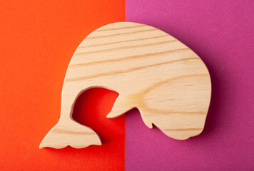 A figurine of a whale carved from solid pine with a hand jigsaw. On a multi-colored background