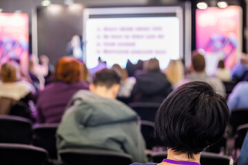 Back view of unrecognizable people, audience listening lecture, presentation at trade show,...