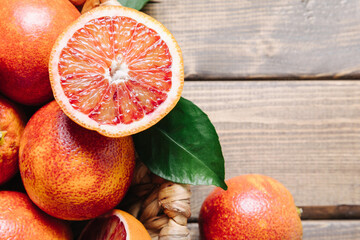 Whole and sliced blood oranges in a basket on wooden table background. Close up, copy space