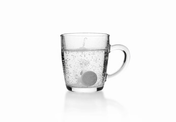 Soluble fizzy tablet on the bottom of transparent glass mug on white background.