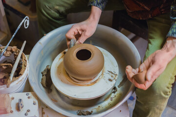 Professional male potter shaping pot with special tool in pottery workshop, studio. Crafting, artwork and handmade concept