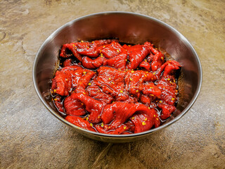 Marinated beef strips in a metal container prepared for drying for a beef jerky