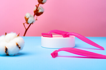 Pink disposable razors and cotton flower on blue paper