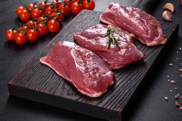 Raw duck breast with herbs and spices on a dark concrete background