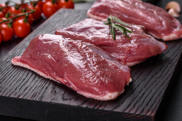 Raw duck breast with herbs and spices on a dark concrete background