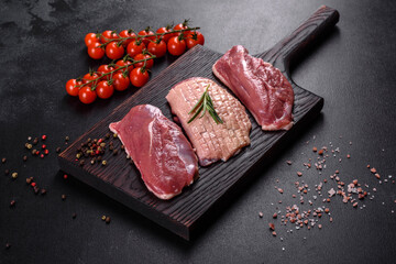 Raw duck breast with herbs and spices on a dark concrete background