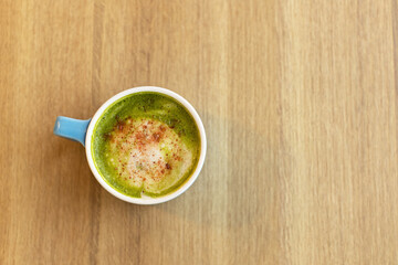 Blue cup with green tea matcha latte, with freeze-dried strawberries on wooden table, copy space. Healthy nutrition concept, drinks with vegetable or cow's milk, vegan beverages. Place for text