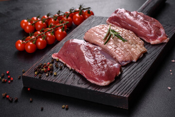 Raw duck breast with herbs and spices on a dark concrete background