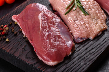 Raw duck breast with herbs and spices on a dark concrete background