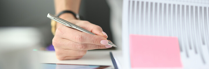 Woman writing with ballpoint pen in documents with graphs and diagrams at table in office closeup