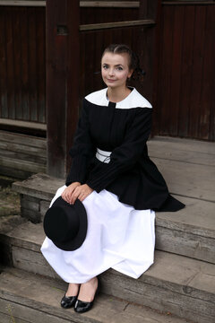 Amish fashion style. Fashion girl wearing stylish black and white dress and hat at countryside. Portrait of pretty woman in village. Stylish amish look. Amish dress. Lifestyle