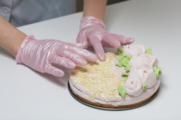 A woman prepares a marshmallow cake. The cake is decorated with marshmallow roses and almond...