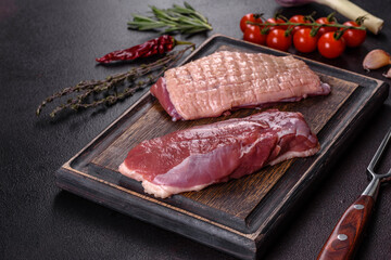 Raw duck breast with herbs and spices on a dark concrete background