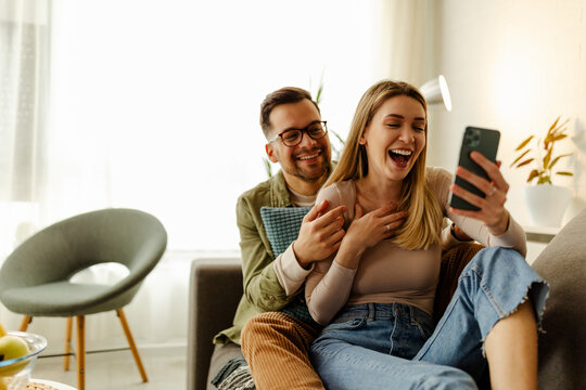 Excited millennial husband and wife relax on couch in kitchen feel euphoric win lottery online.