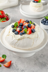 Pavlova meringue cake with whipped cream and fresh berries on top on a plate on a gray concrete background. Summer dessert. Copy space.