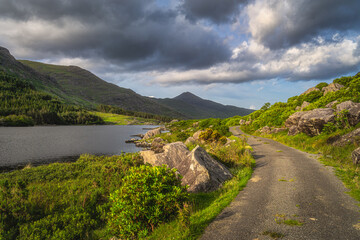 Winding country road leading trough Black Valley. Landscape illuminated by sunlight at sunset, MacGillycuddys Reeks mountains, Ring of Kerry, Ireland
