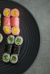 Kawałki sushi hosomaki na czarnym talerzu owinięte różowym nori
