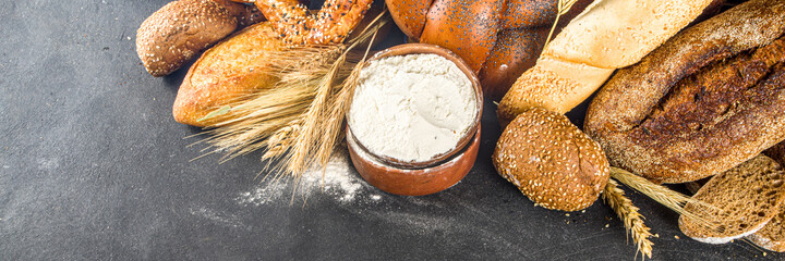 Assortment of various delicious freshly baked bread, on black concrete background top view copy space