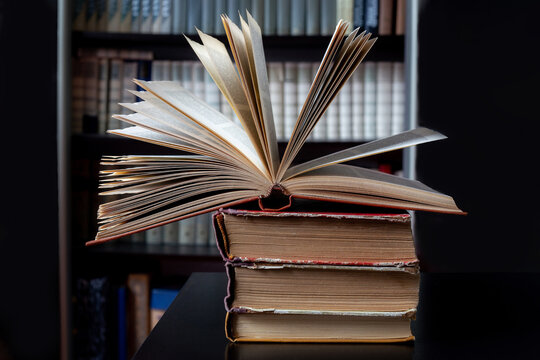 open book sits on a stack of old, battered books, with shelves of books in the background