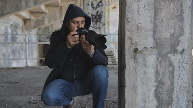 A man secretly takes photos with a long-focus lens while hiding in an abandoned building.