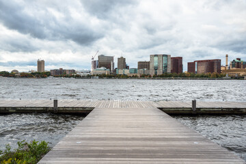 Deserted wooden pier on a wide river with an urban skyline in background on a stormy autumn day....