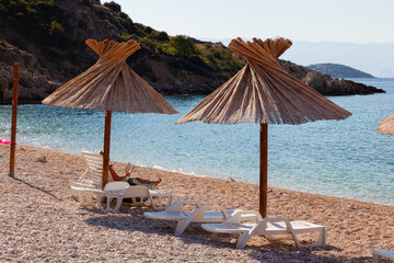 Girl relaxing on the deck chair while reading a book under a straw umbrella in the Oprna beach, Krk island