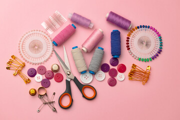 Fototapeta na wymiar Sewing accessories including thread spools and pins on pink background