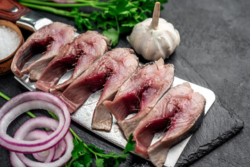 pieces of pickled herring on a knife with onions and herbs on a stone background