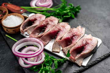 pieces of pickled herring on a knife with onions and herbs on a stone background