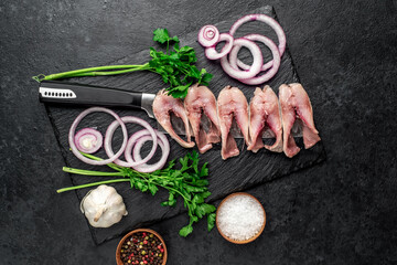 pieces of pickled herring on a knife with onions and herbs on a stone background