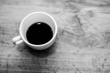 Black and white textured photo; close-up of ceramic cup with coffee on wooden table.