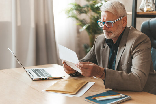 An Invoice For Payment. Attentive Senior Man Looking At Bank Statement, High Taxes. Check For Payment Of Money.