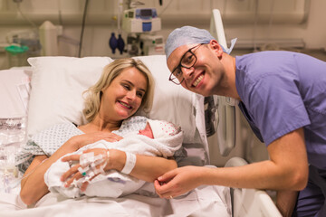 A pregnant woman in a maternity hospital holds a newborn in her arms. Lying on the bed. Her husband supports her after birth.