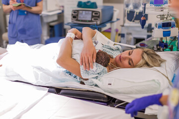 A pregnant woman in a maternity hospital holds a newborn in her arms. Lying on the bed.