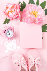 Newborn greeting card. Pink baby clothes with shoes and peony on pink background. Copy space. Vertical format.