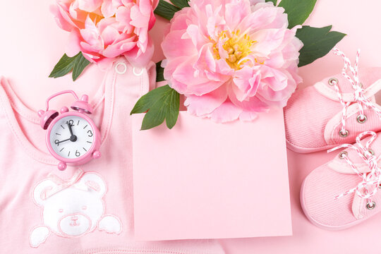 Newborn greeting card. Pink baby clothes with shoes and peony on pink background. Copy space.