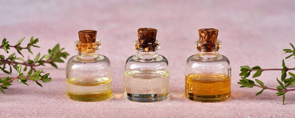 Essential oil bottles with fresh thyme twigs on pastel pink background