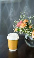 Paper cup with coffee and a bouquet of fresh flowers