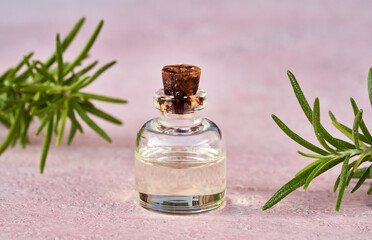 Essential oil bottle with fresh rosemary on pink background